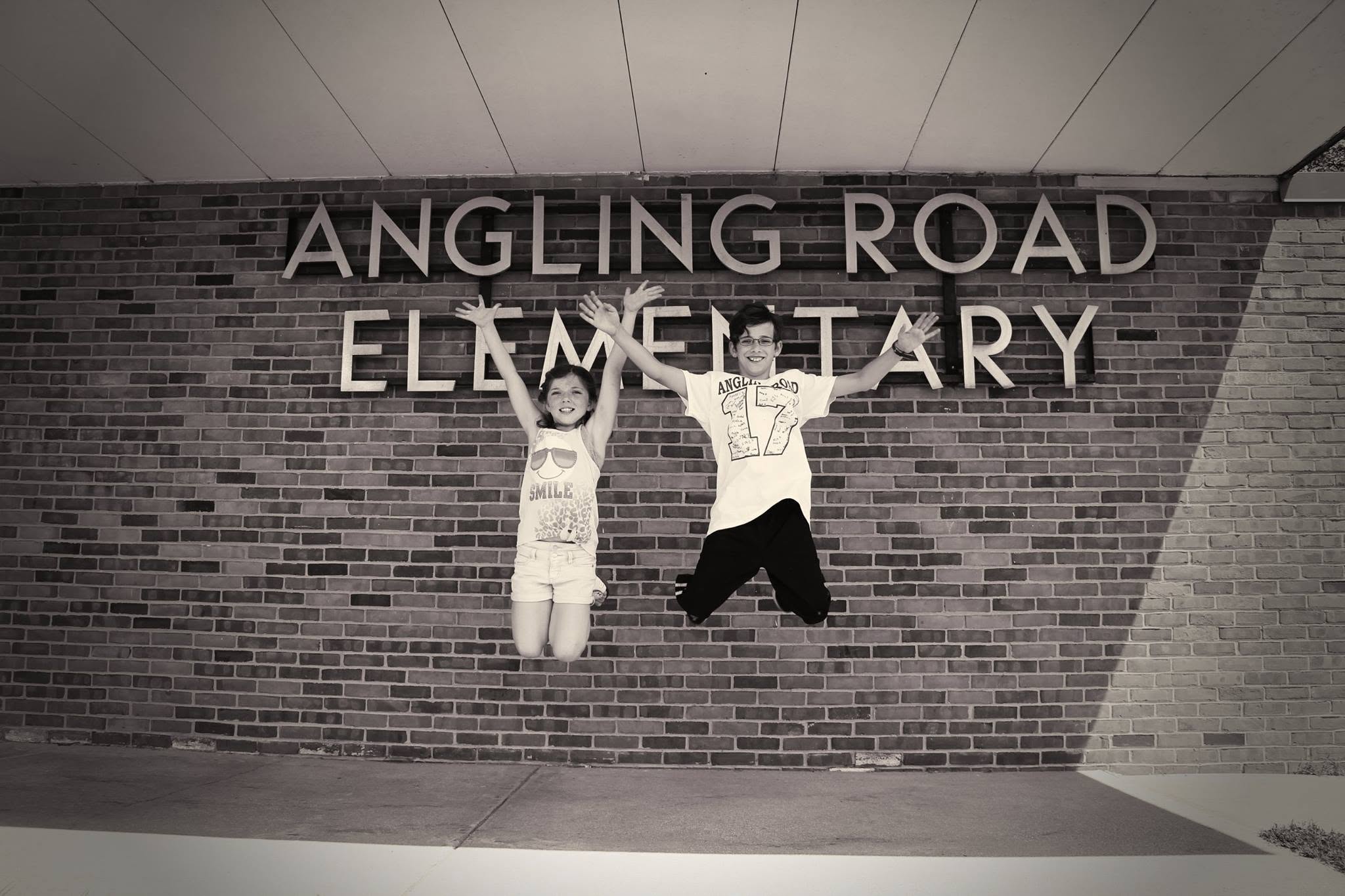 Heather's kids jumping in front of the Angling Road Elementary sign, a favorite yearly photo